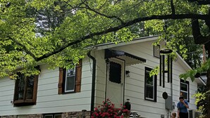 A two-story house with a stone foundation, white siding, and a porch with red flowers.