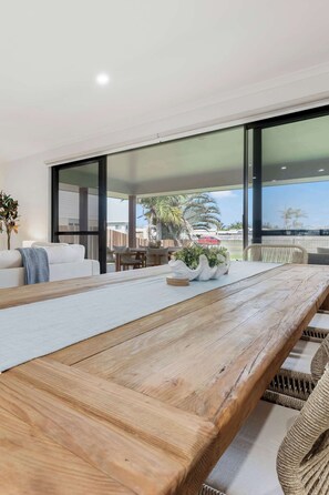 A spacious room with a wooden dining table, white sofa, and wicker chairs. - Burnett Heads Beach Family Escape (Burnett Heads)