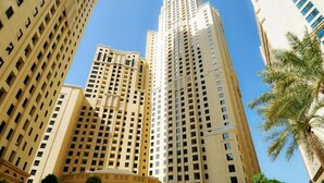 A high-rise building with multiple floors, a central entrance, and surrounding greenery.