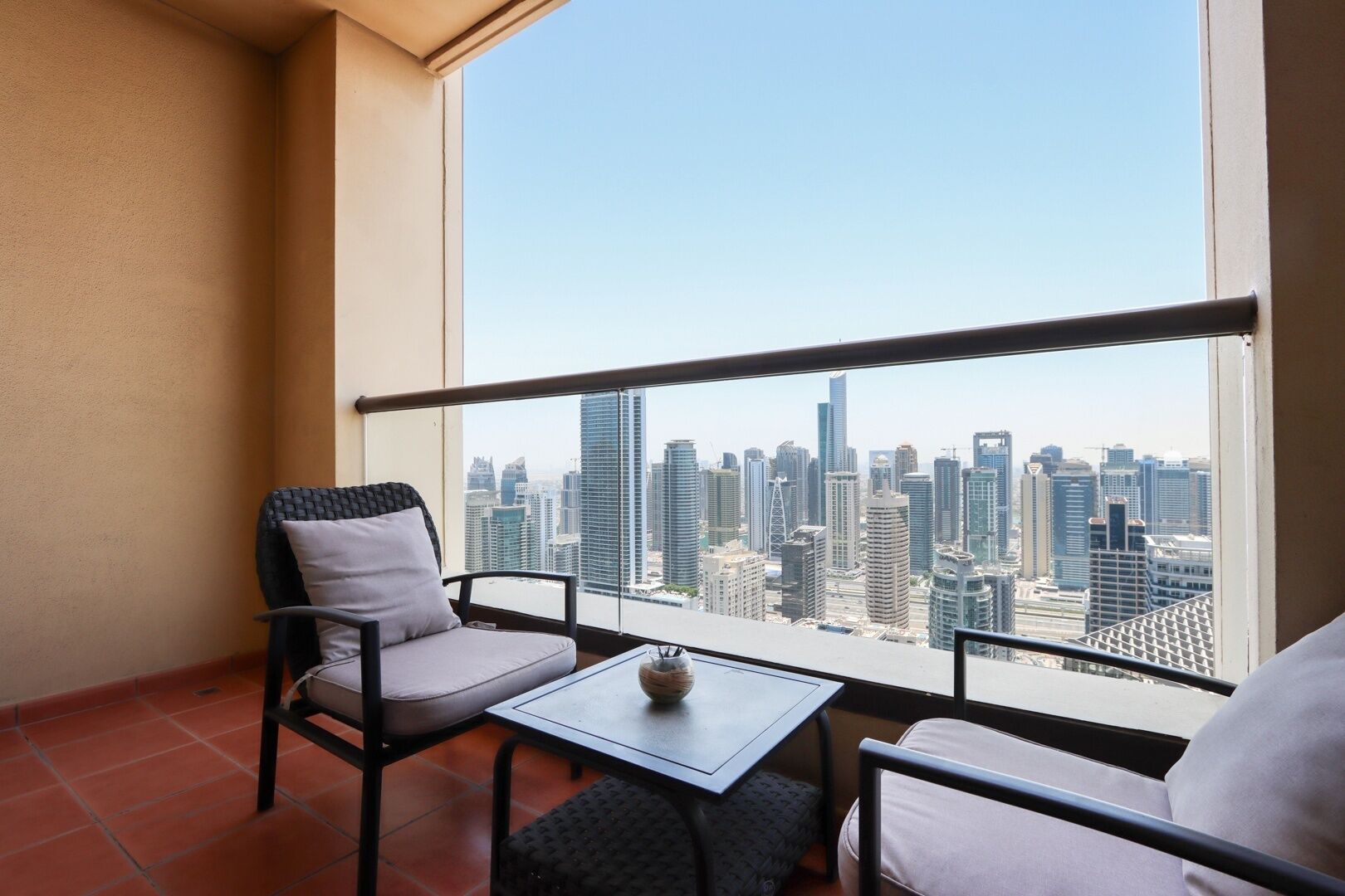 A balcony with two chairs and a small table, overlooking a cityscape with tall buildings.