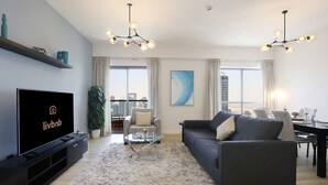 A modern living room with a flat-screen TV, grey sofa, and a city view. - Sleek 2BR w Marina Skyline Views | Dubai Marina (Dubai)