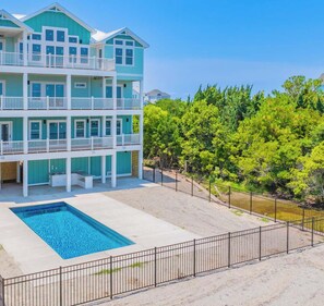 A multi-story beachfront property with a swimming pool, balconies, and a fenced yard.