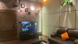 A living room with a brick wall, a television, a leather sofa, and a small wooden table. - welcome apartment (Jeddah)