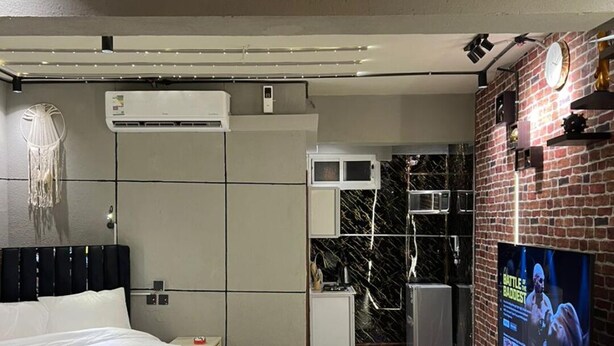 A modern hotel room with a large bed, a flat-screen TV, a fireplace, and a brick accent wall. - welcome apartment (Jeddah)