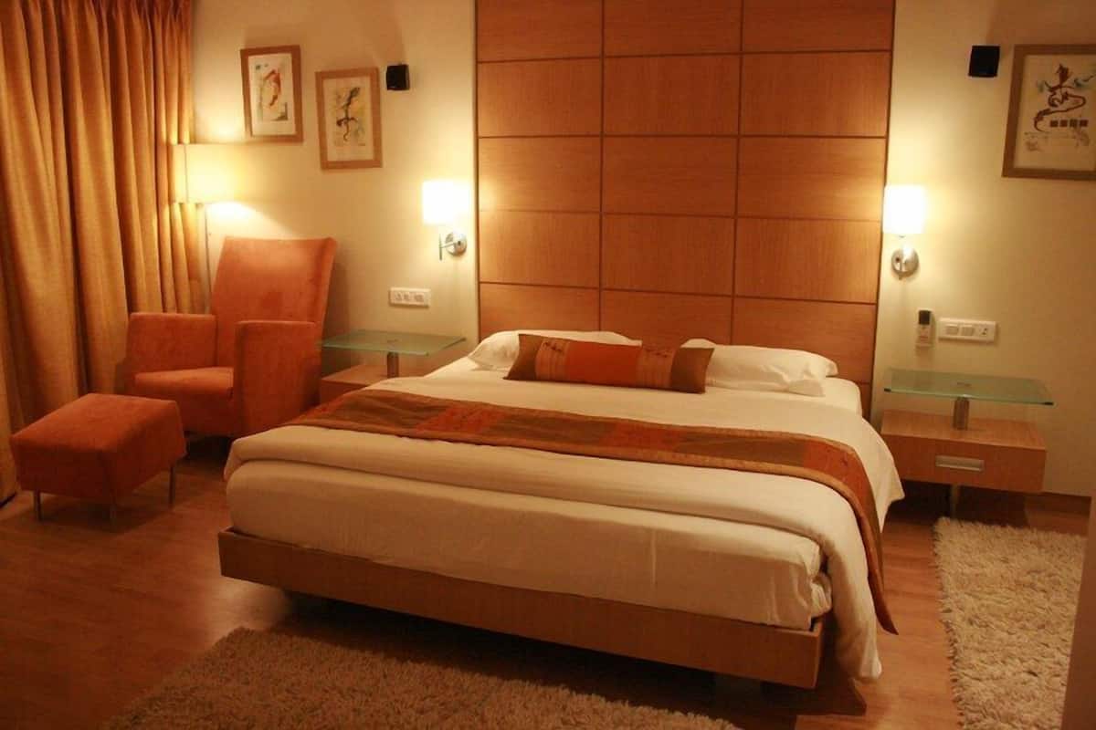 A modern hotel room with a large bed, a seating area with chairs, and a wooden headboard.