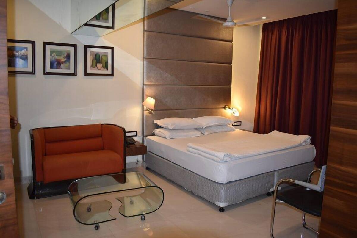 A modern hotel room with a bed, a glass coffee table, an orange sofa, and framed pictures on the wall.