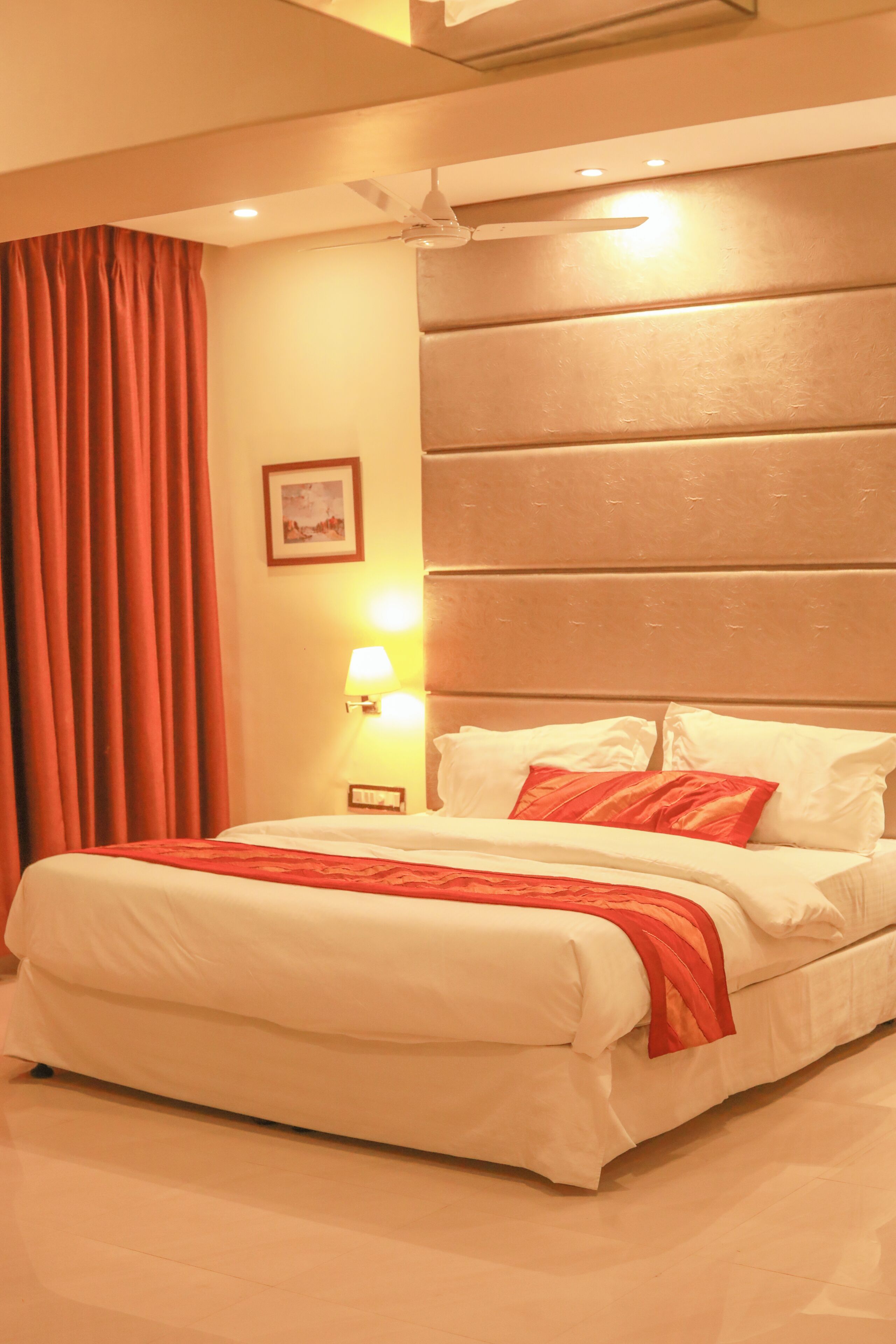 A hotel room with a large bed, a ceiling fan, and a wall-mounted lamp.
