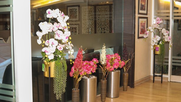 A reception area with vases of orchids and a reception desk. - Hr Residency (Mumbai)
