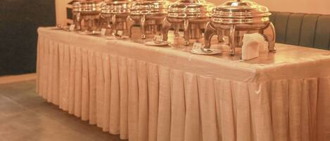 Una larga mesa con varios platos de plata alineados, frente a una pared con diseños decorativos en las ventanas.
