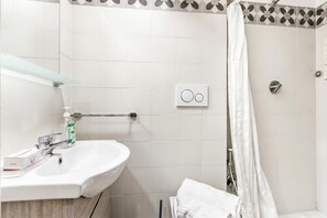 Une salle de bain avec un lavabo blanc, une étagère en verre, une serviette et un rideau de douche.