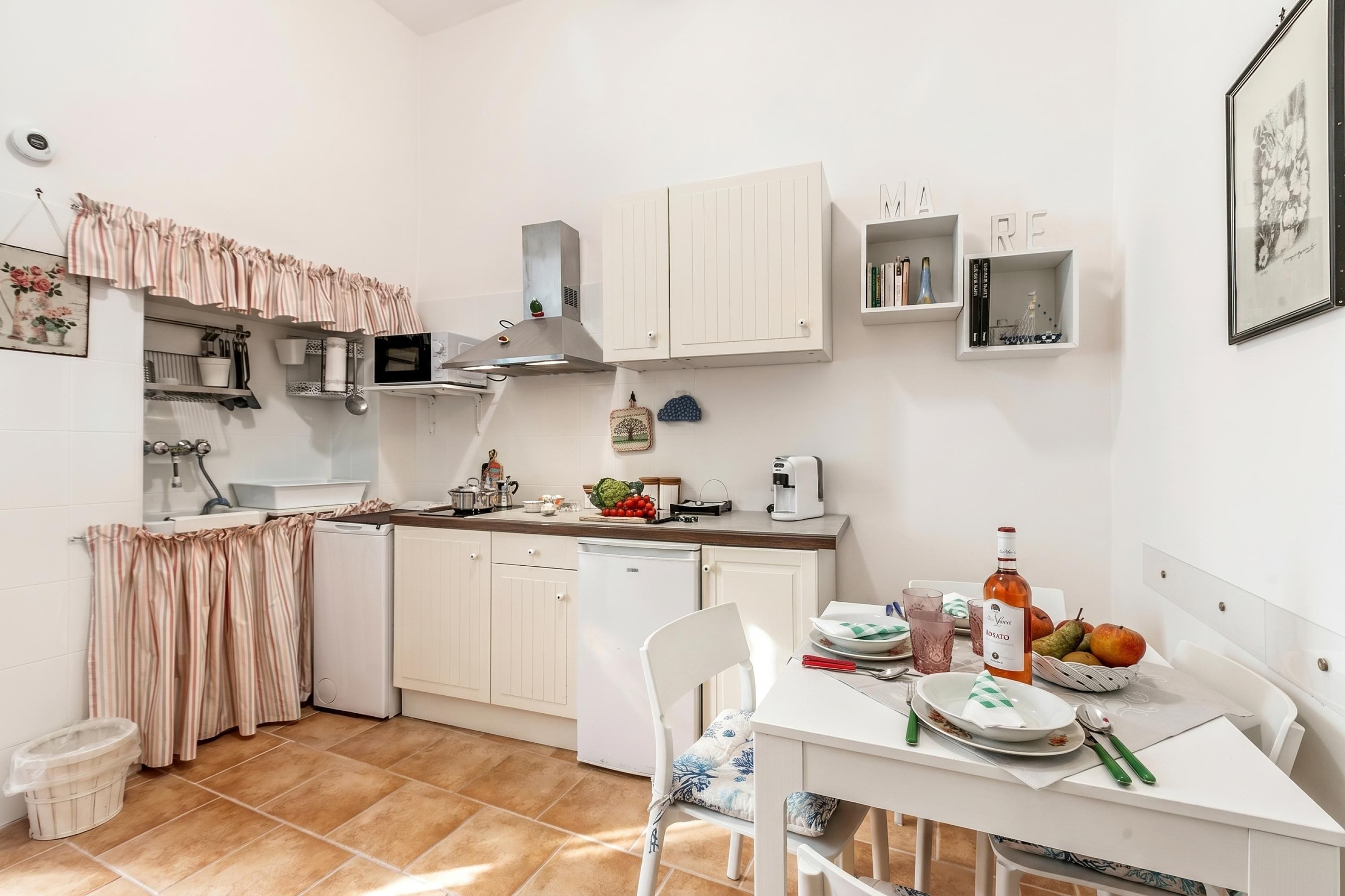Een kleine keuken met witte kastjes, een eettafel en een kleine koelkast.
