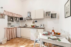 Eine kompakte Küche mit weißen Schränken, einem Esstisch und einem kleinen Kühlschrank.