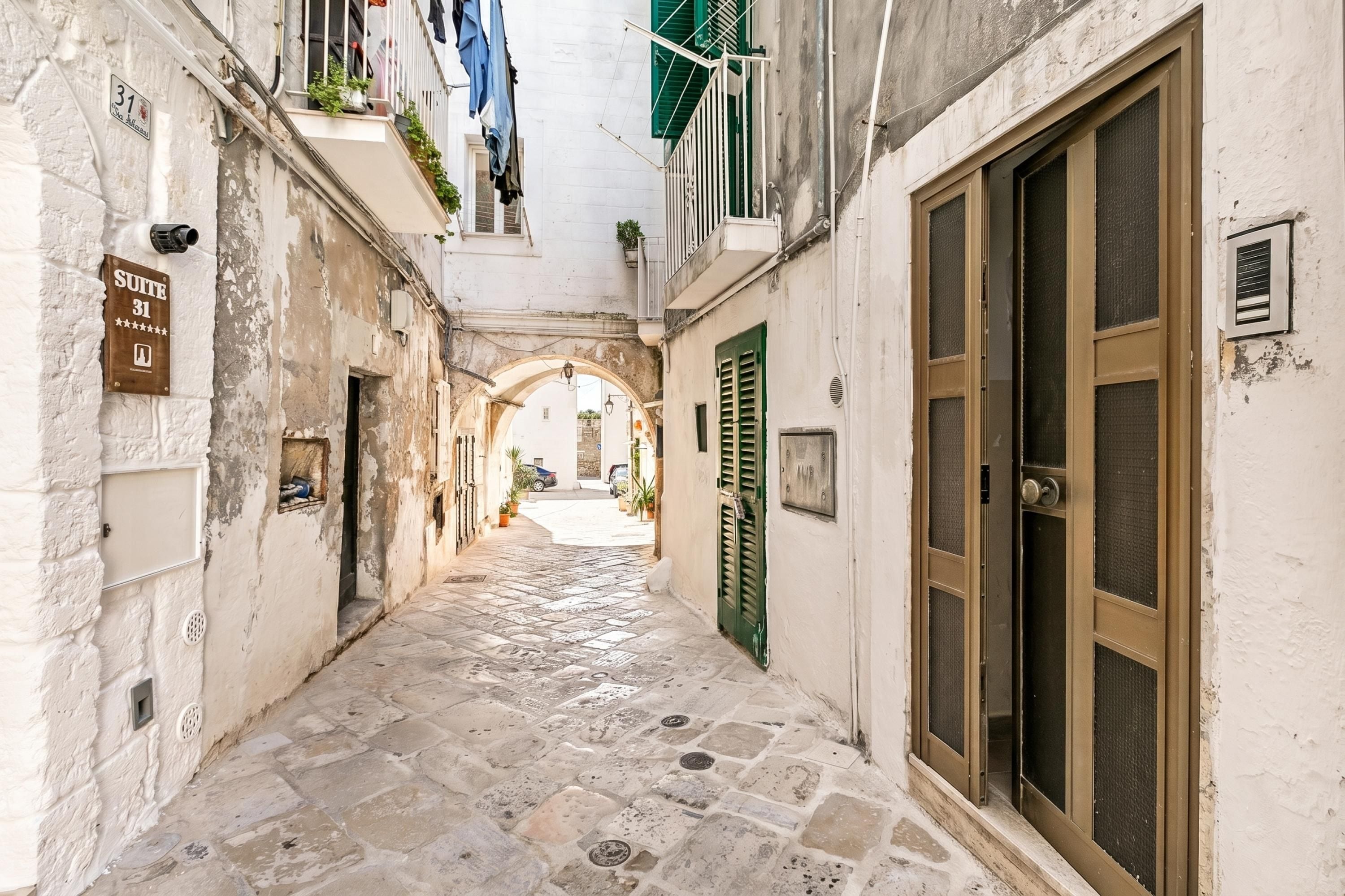 A narrow stone-paved alleyway with a sign for 'Suite 31' and a large window with a metal grill.