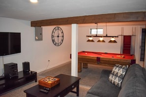Una sala de estar con mesa de billar, un sofá, una televisión y un reloj en la pared.