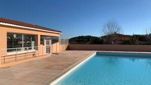 A swimming pool with a tiled deck, a building with large windows, and a clear sky. - French Riviera Villa (Biot)