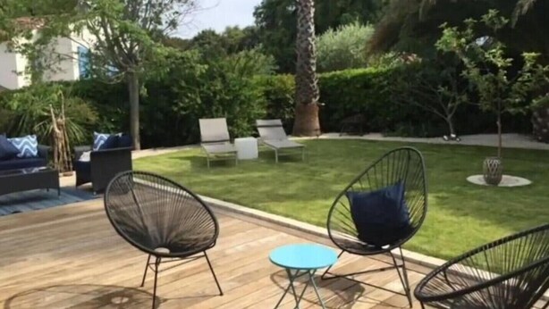 An outdoor patio with a wooden deck, surrounded by lush greenery and a well-maintained lawn. - French Riviera Villa (Biot)