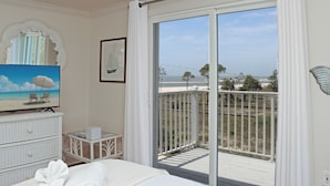 Une chambre avec une grande porte-fenêtre coulissante donnant sur un balcon, un lit, une commode, un téléviseur et un tableau encadré.