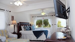 Une chambre à coucher avec un lit, une chaise, un bureau, un téléviseur et une fenêtre avec des rideaux.
