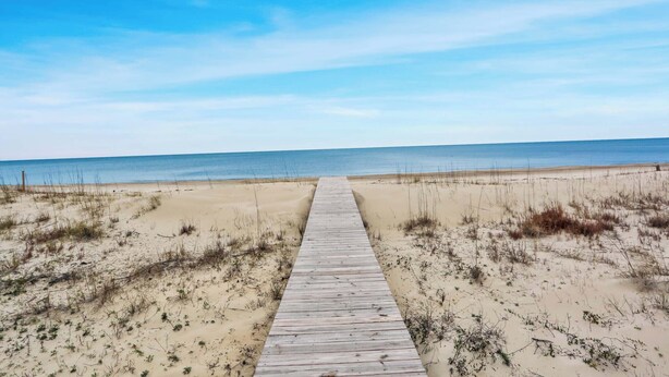 Une promenade en bois menant à une plage bordée de dunes de sable et d’une végétation clairsemée.