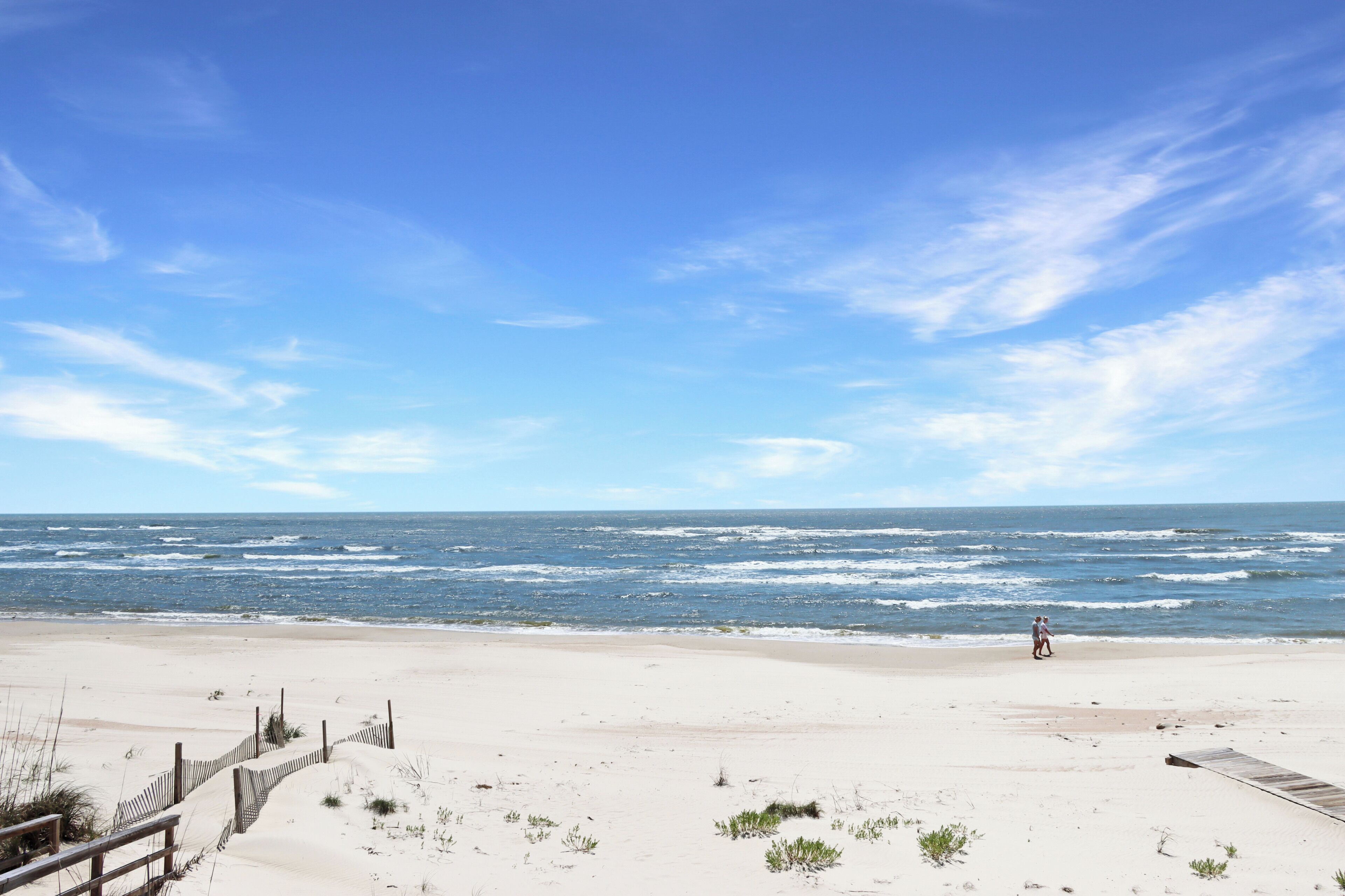 A beach with a wooden boardwalk, sandy dunes, and the ocean in the background.