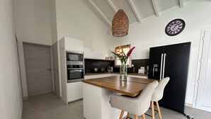 Une cuisine moderne avec des meubles blancs, un plan de travail en bois, un réfrigérateur noir et une horloge au mur.