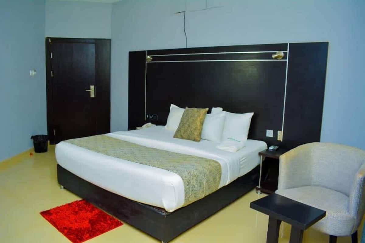 A hotel room with a large bed, a bedside table, a chair, and a red rug.