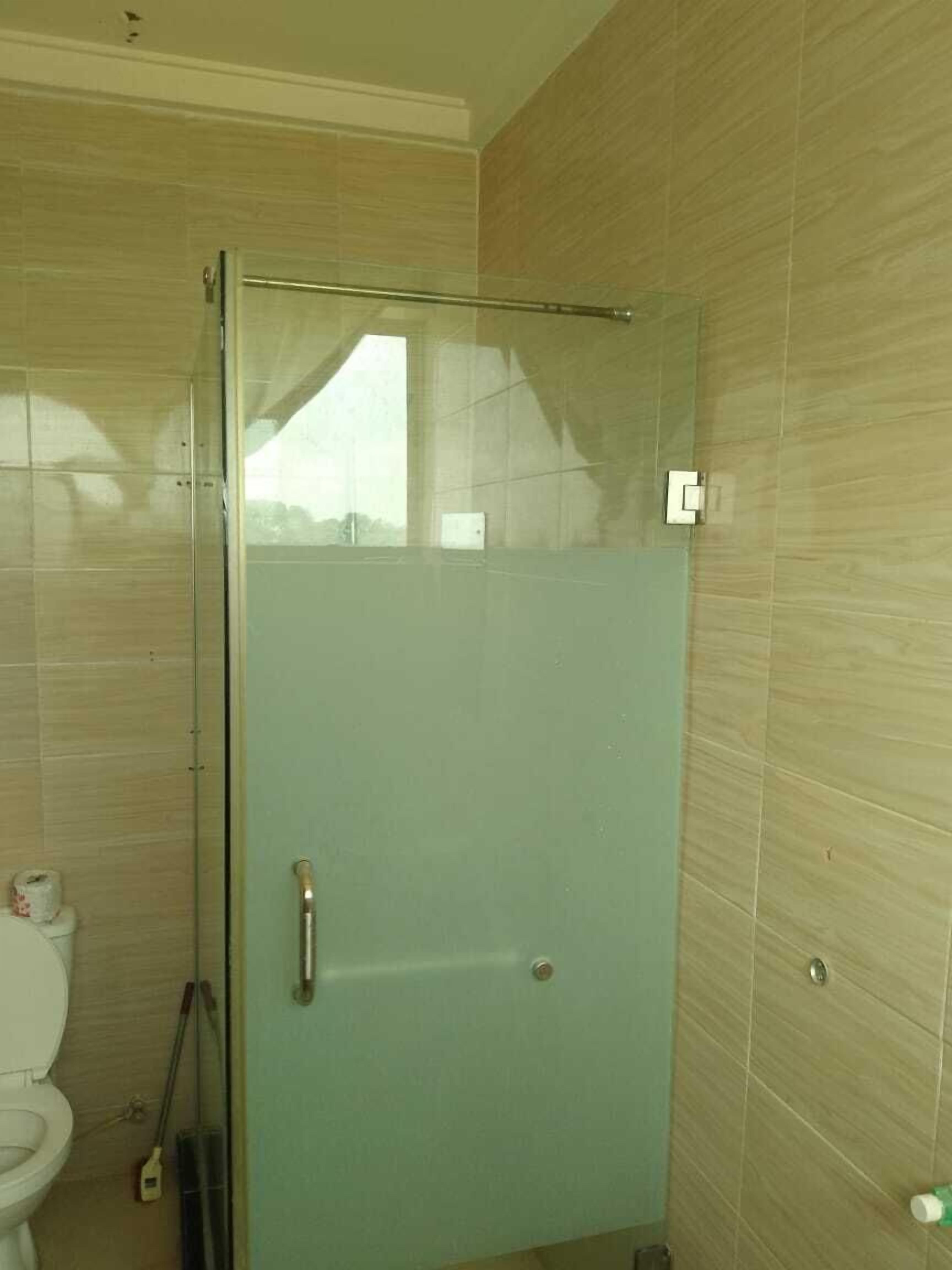 Un baño con cabina de ducha de vidrio, un inodoro y una mopa apoyada en la pared.