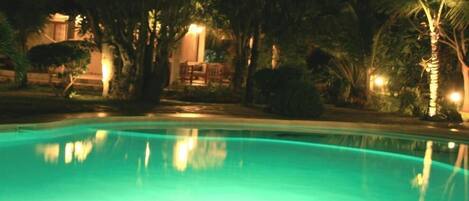 A nighttime view of a swimming pool with a clear water surface reflecting surrounding lights.