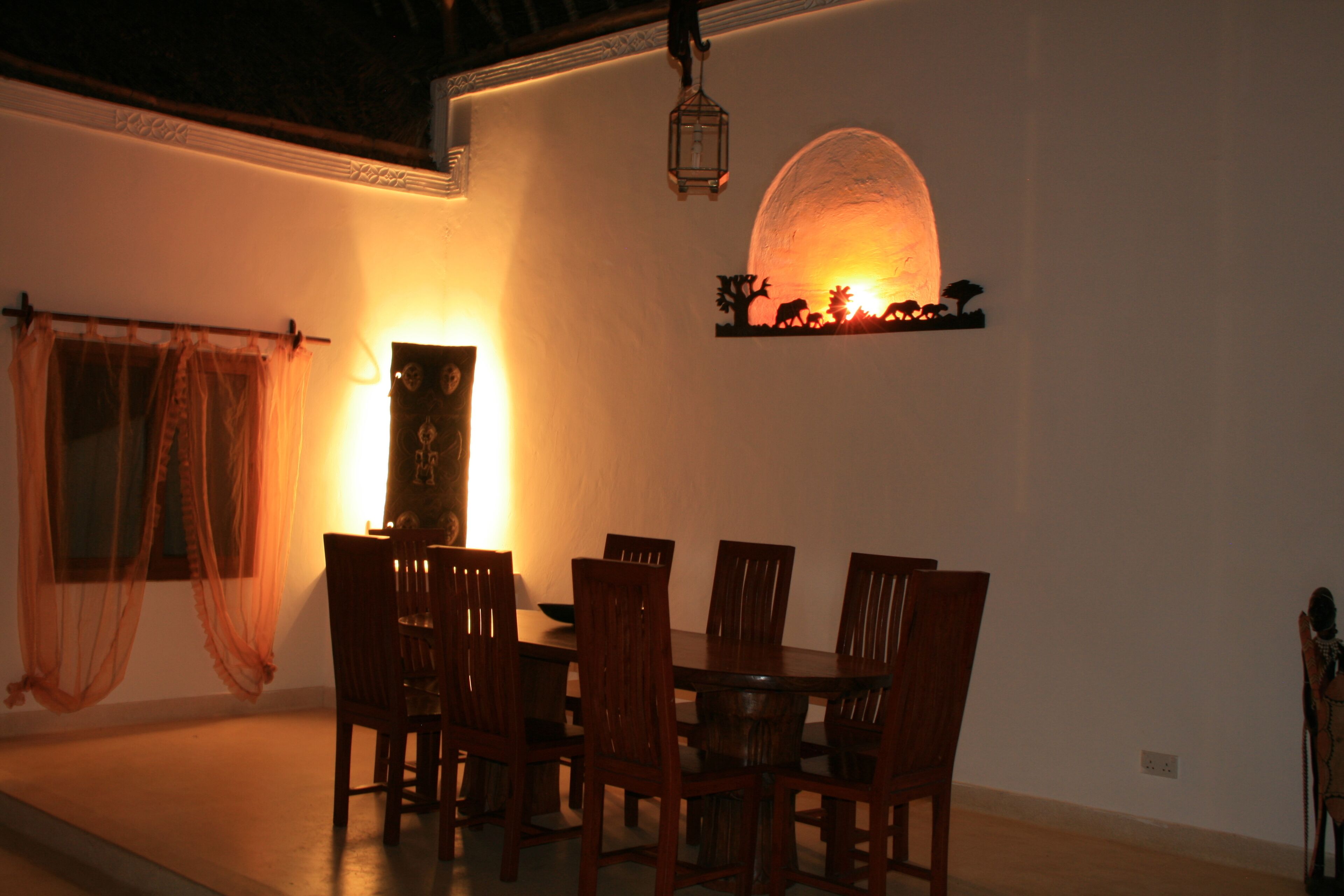 A dining area with a round table and six chairs, a decorative wall shelf, and a hanging lantern.
