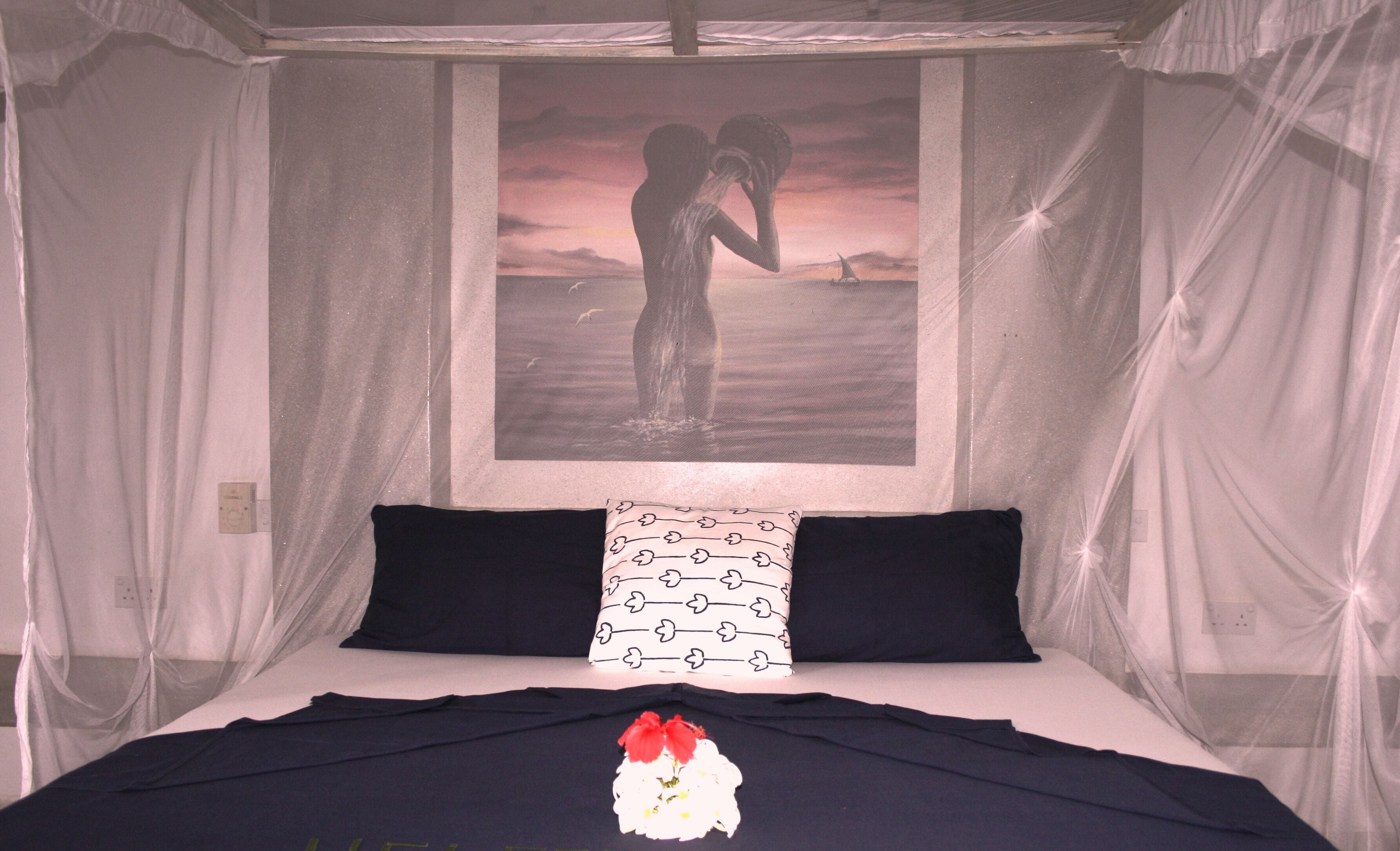 Una cama con dosel, dos almohadas y un cuadro con una pareja en la playa.