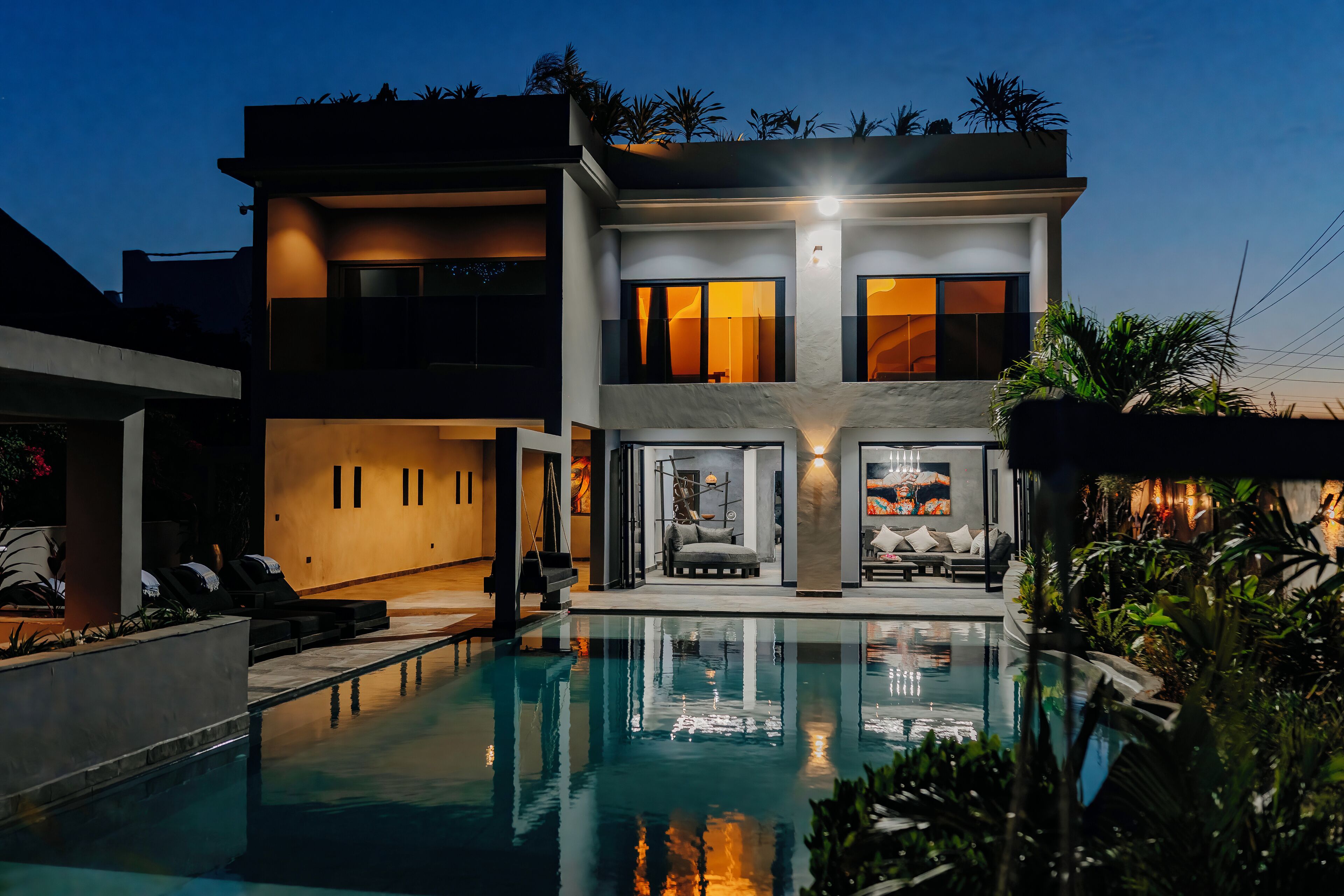 Una casa moderna de dos pisos con piscina, mobiliario exterior y un interior bien iluminado.