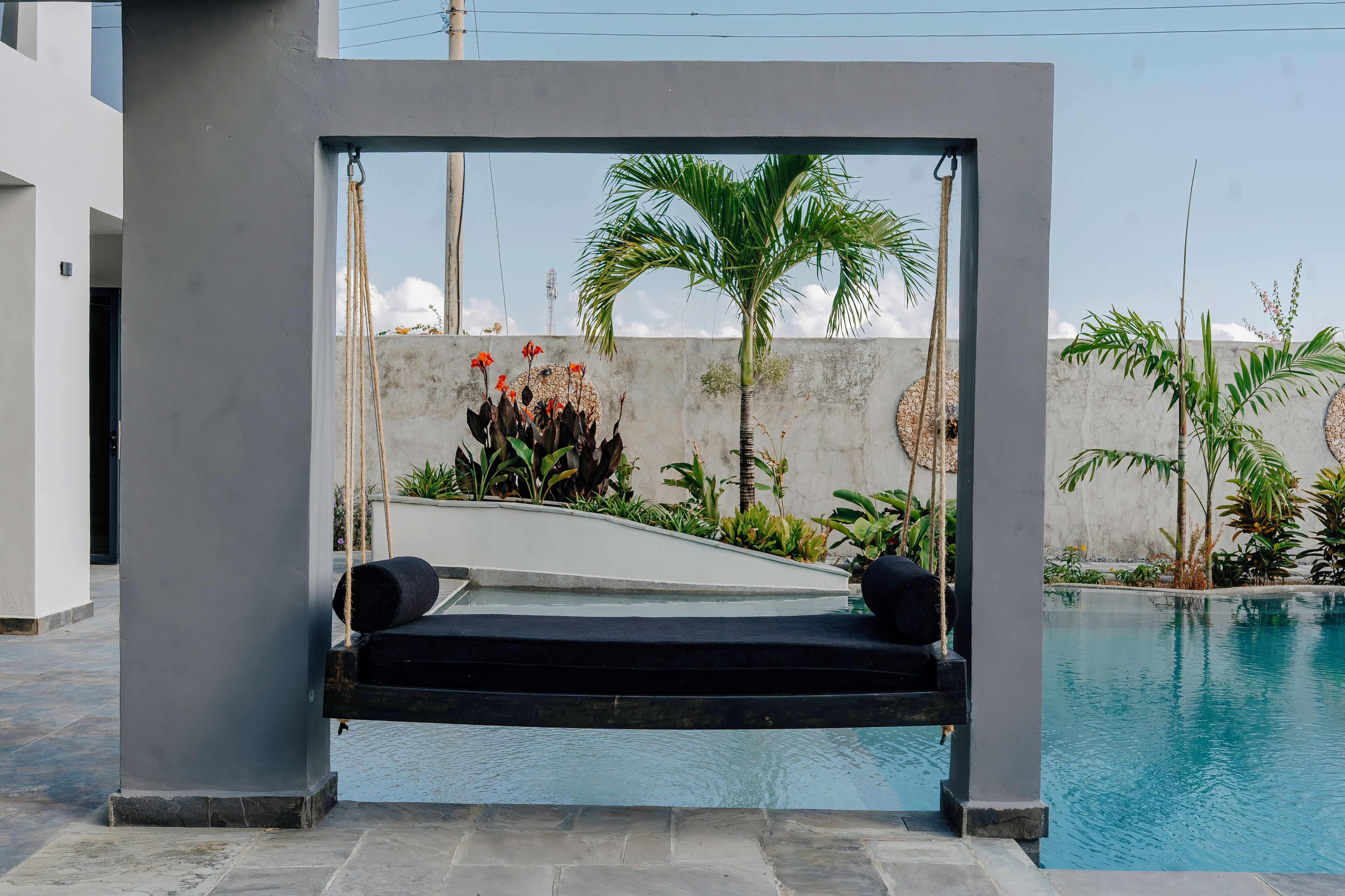 A modern outdoor seating area with a swing, a pool, and tropical plants.