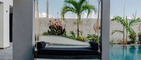 A modern outdoor seating area with a swing, a pool, and tropical plants.