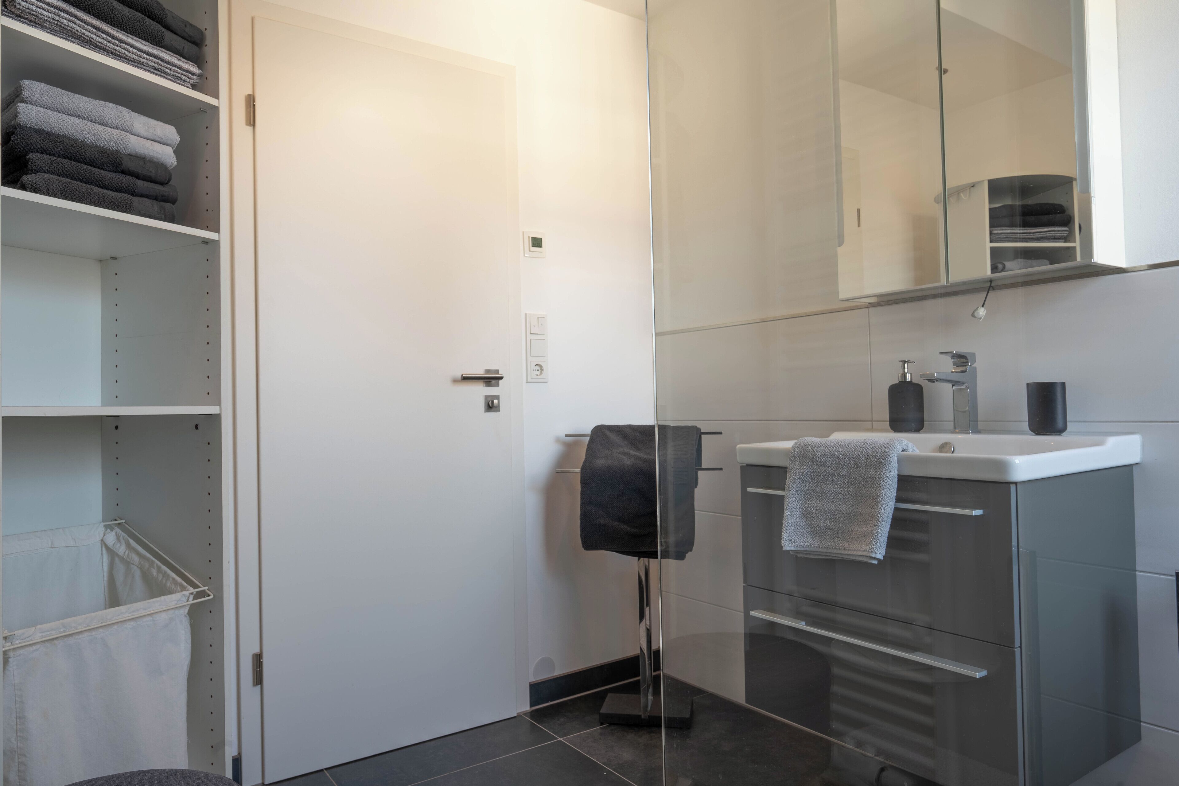 A modern bathroom with a glass shower enclosure, a white sink with a towel, and a storage cabinet.