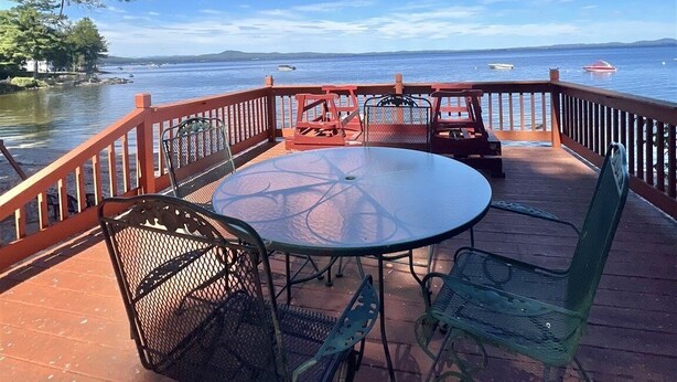 Una terraza con una mesa redonda de vidrio y sillas de metal, con vista a un cuerpo de agua con barcos.