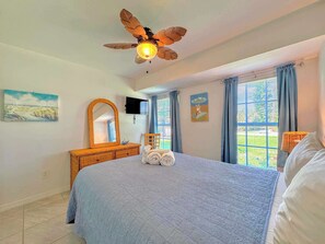 Une chambre à coucher comprenant un lit, un ventilateur de plafond, une commode, un téléviseur et des œuvres d’art accrochées aux murs.