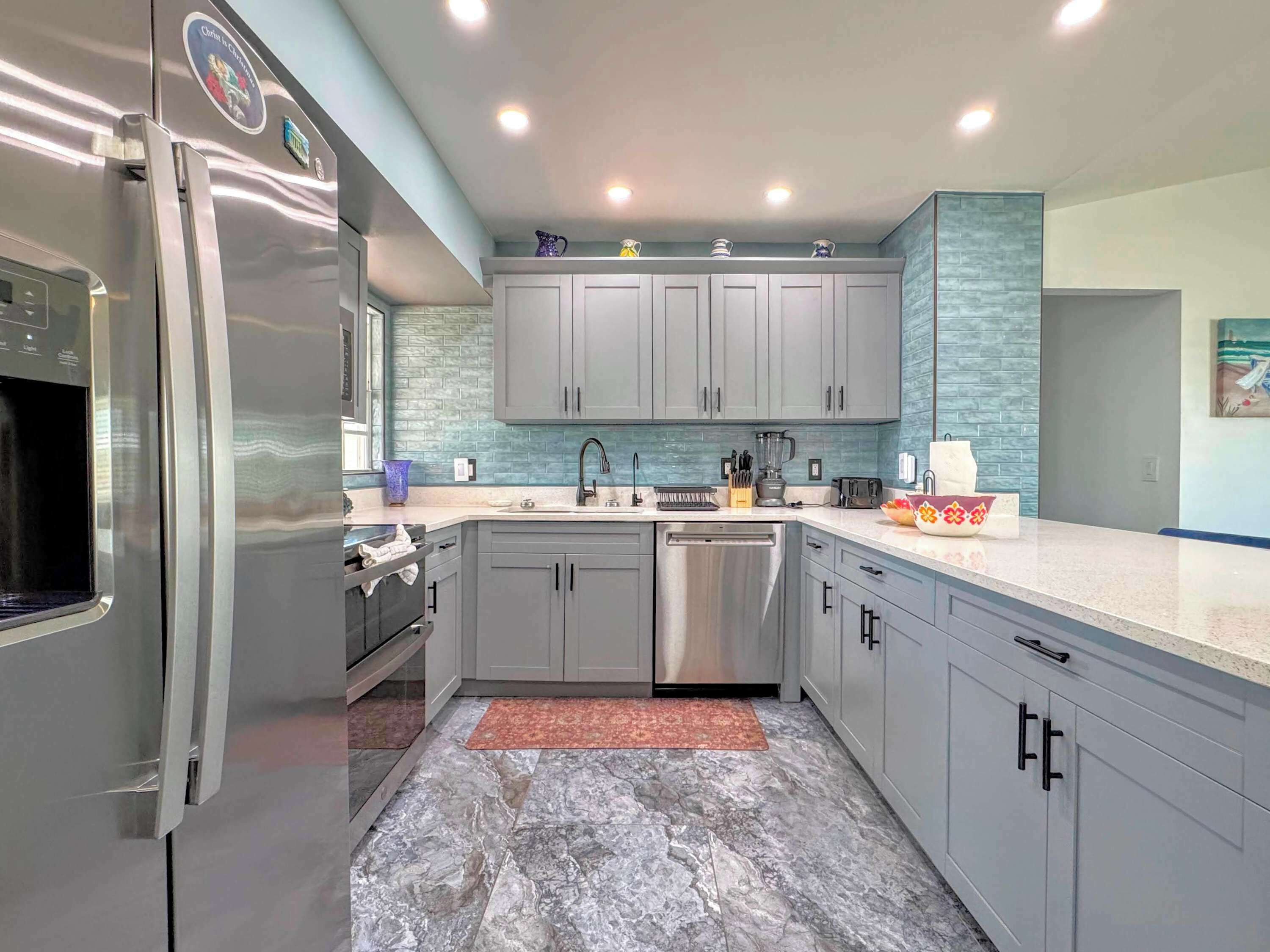 A modern kitchen with grey cabinets, a stainless steel refrigerator, a dishwasher, and a granite countertop.