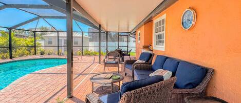 An outdoor patio with a pool, wicker furniture, and a covered area with a view of the neighborhood.