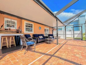 Ein überdachter Patio-Bereich mit Korbmöbeln, einer Bar und Blick auf ein Nachbarhaus.