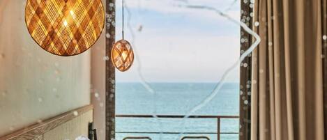 A hotel room with a bed, a view of the sea, and a hanging light fixture.