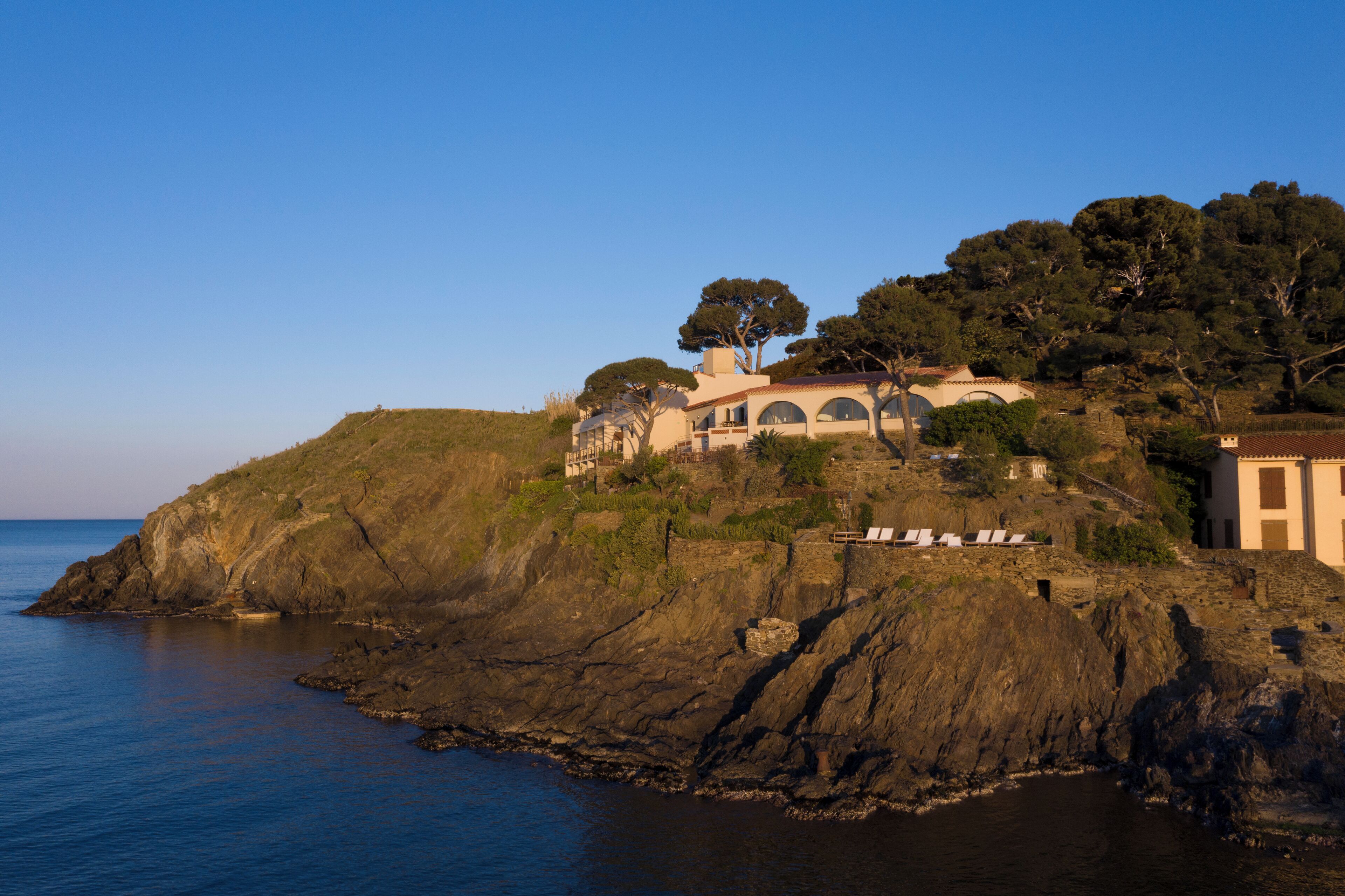 A coastal property with a large house on a cliff, overlooking the sea.