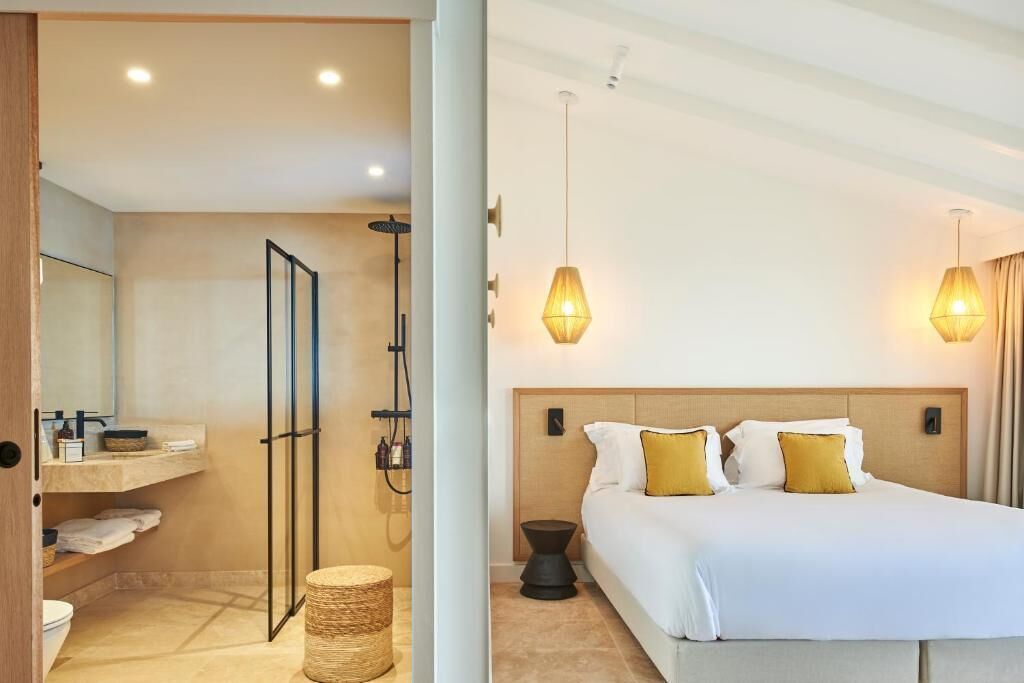 A modern hotel room with a large bed, two bedside lamps, a wooden headboard, and a small bedside table.