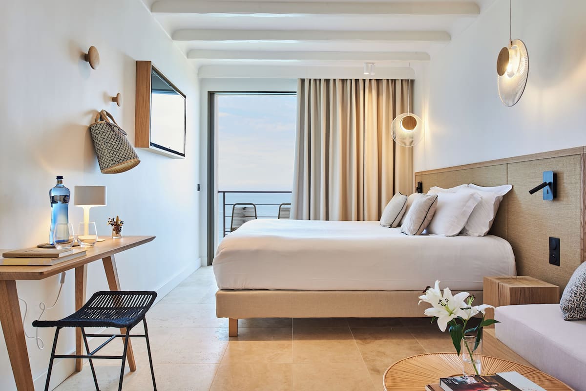 Habitación de hotel moderna con una cama grande, un escritorio con silla, una mesita con un florero y vistas al exterior.