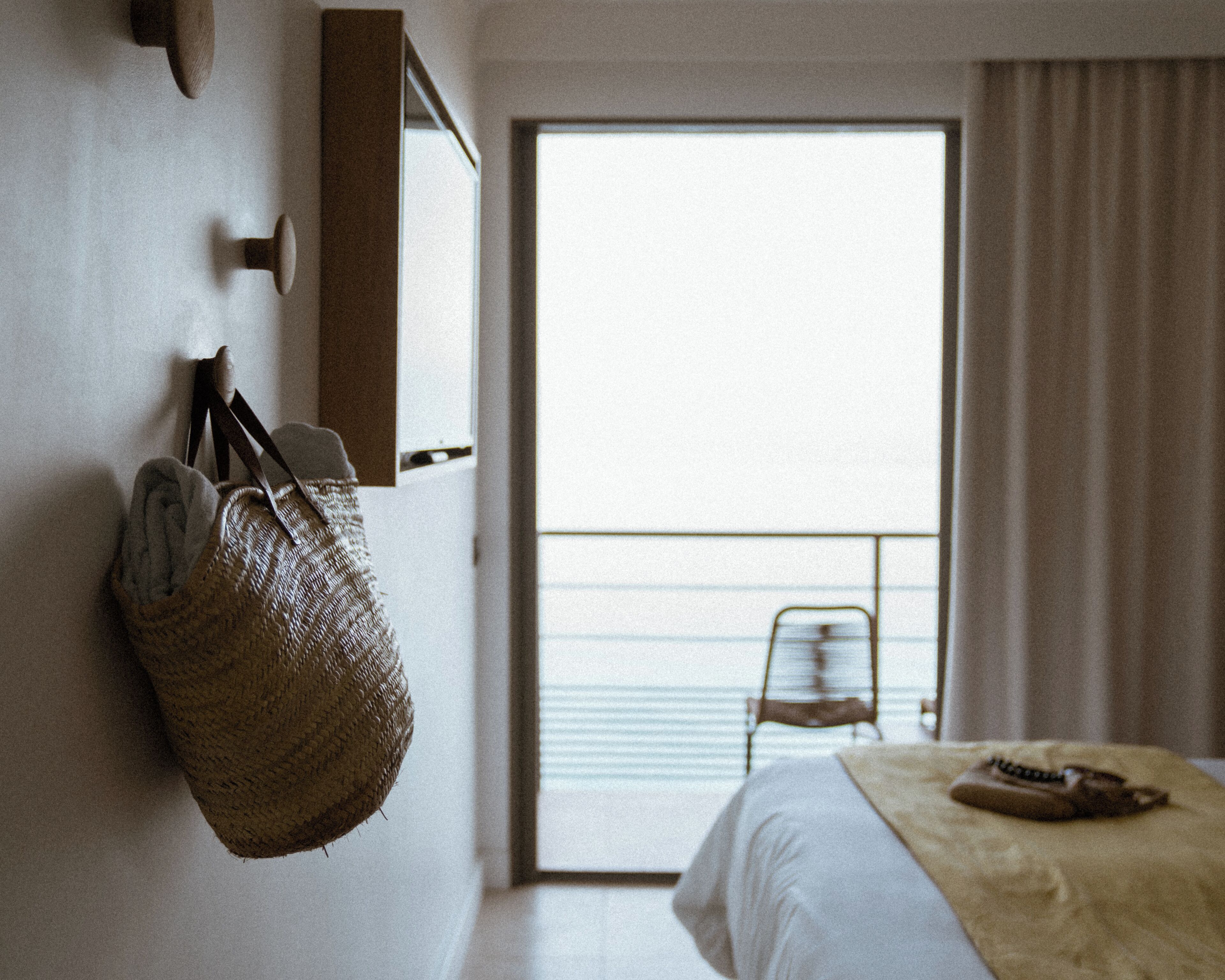 Une chambre d’hôtel avec un lit, une suspension décorative, une chaise et une vue sur la mer par une grande fenêtre.