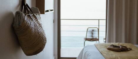 A hotel room with a bed, a hanging basket, a chair, and a view of the sea through a large window.