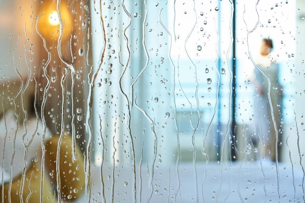 A window with raindrops, blurred background, and a person visible.