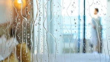 A window with raindrops, blurred background, and a person visible.
