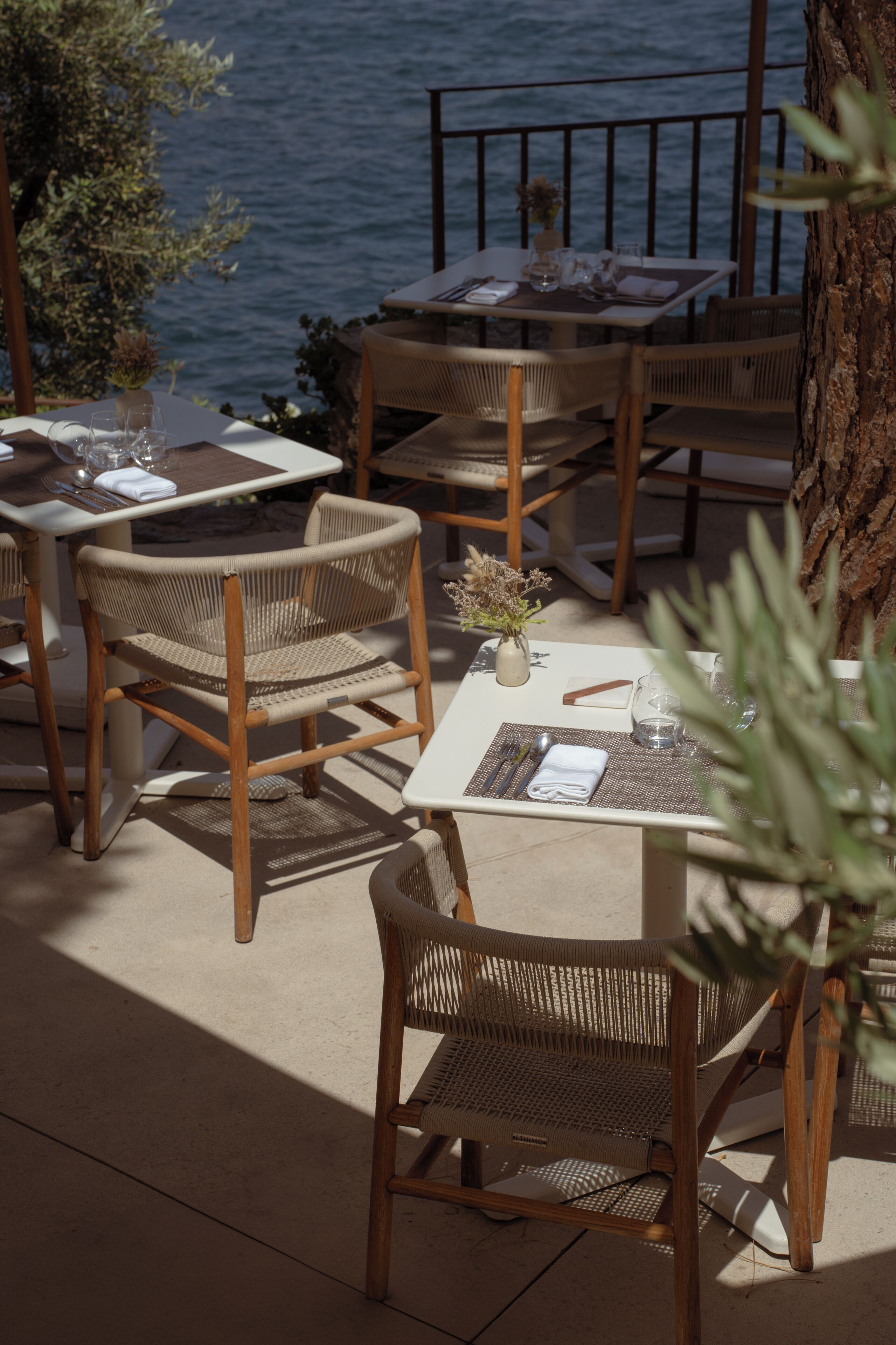A terrace with wicker chairs and tables, overlooking a body of water.
