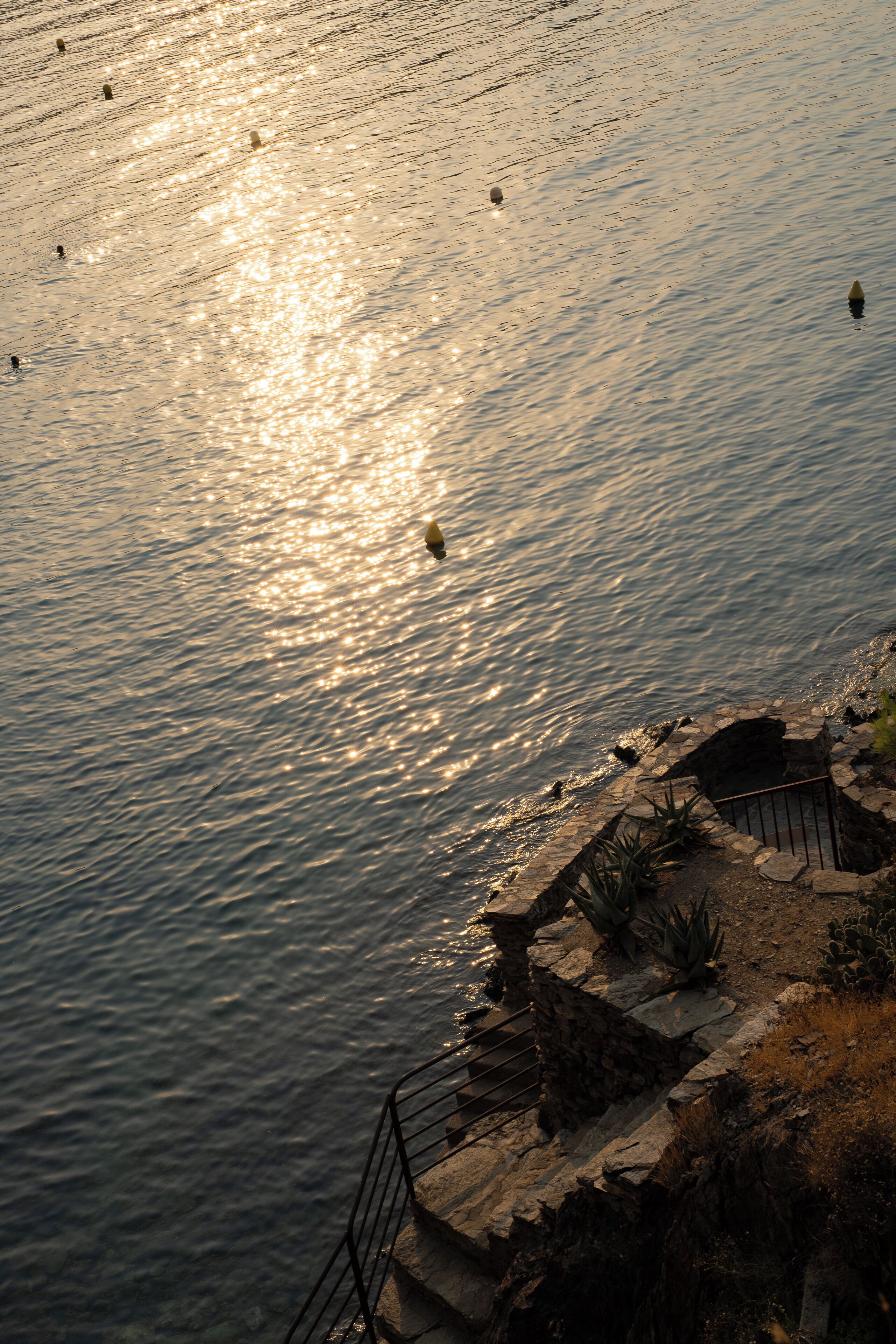 A stone pathway leading to a body of water with reflections of the sun.