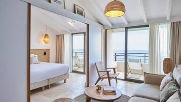 Una habitación de hotel moderna con una cama, un sofá, una mesita redonda y un balcón con vistas al mar.